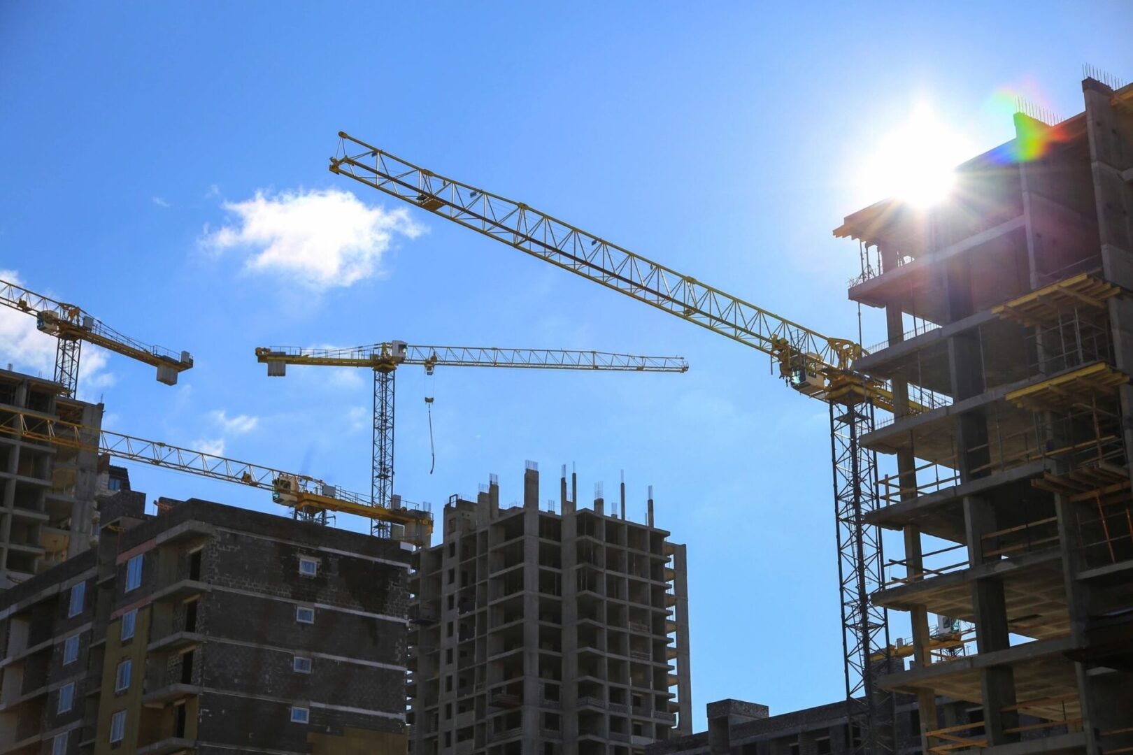 Construction site with multiple cranes and buildings under construction against a clear blue sky.
