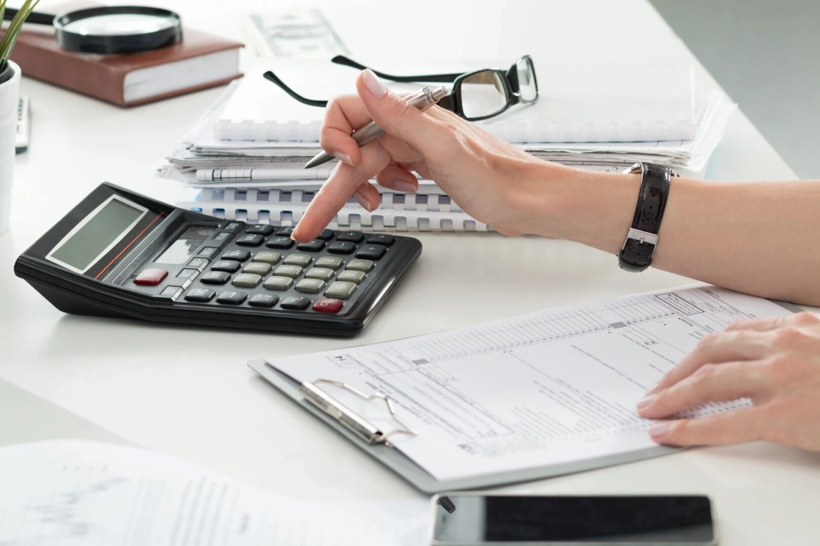 Person calculating finances using a calculator at a desk with paperwork.