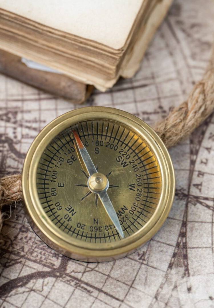 Vintage compass on an old map with a bound rope and book in the background.