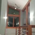 Modern interior hallway featuring wooden beams, a high ceiling with a ceiling fan, and horizontal railings.